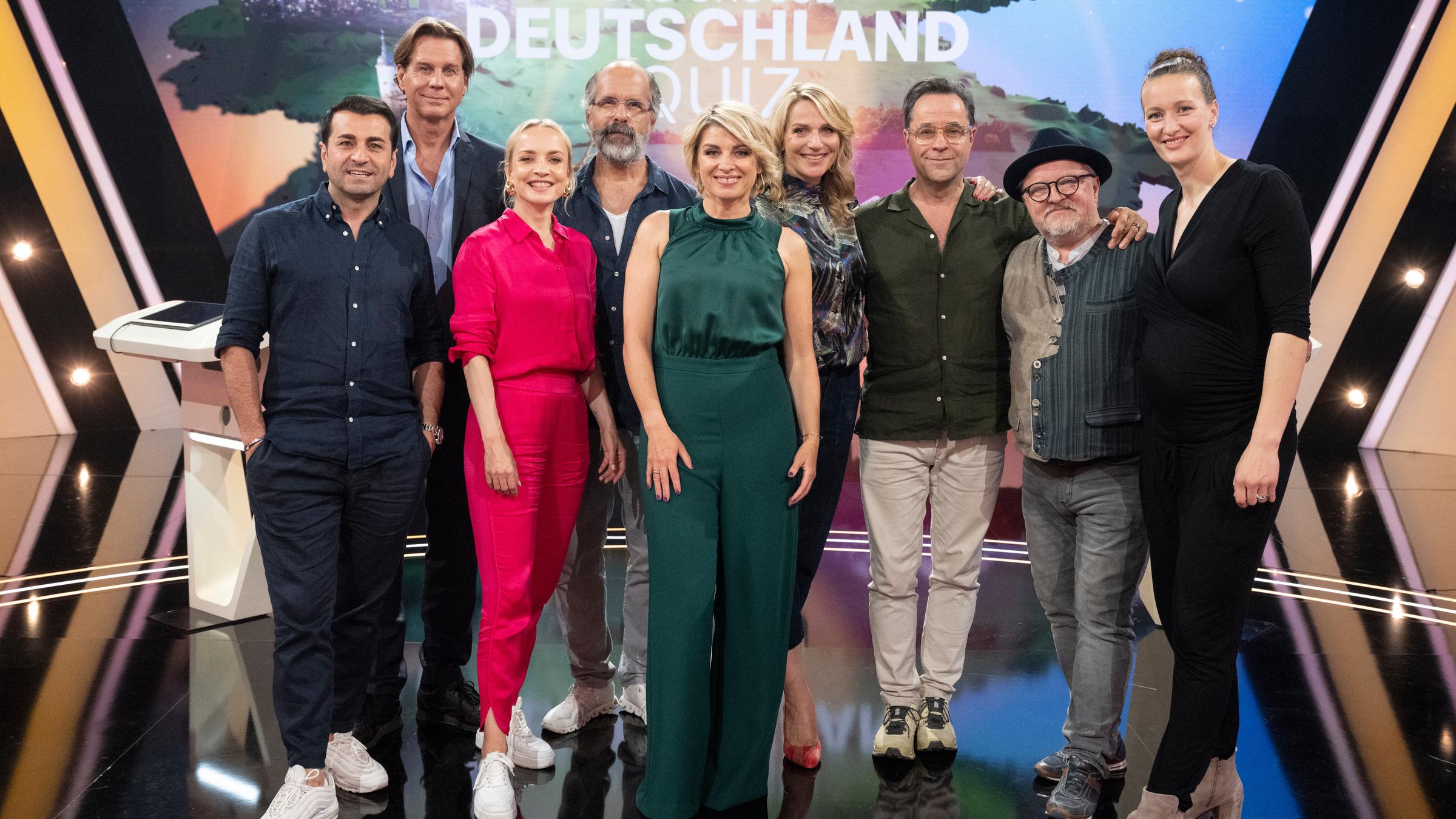 "Das große Deutschland-Quiz": Ali Güngörmüs, Thomas Heinze, Janin Ullmann, Christoph Maria Herbst, Sabine Heinrich, Tanja Wedhorn, Jan Josef Liefers, Axel Prahl und Almuth Schult stehen zusammen vor dem Sendungslogo.