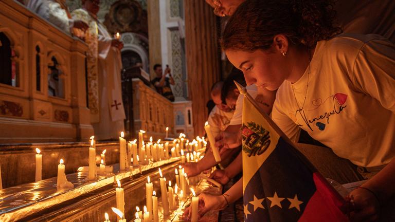 Ein Mädchen zündet eine Kerze während einer Messe an. Vor ihr stehen viele weitere Kerzen zu Gedenken an die Erdbebenopfer in Venezuela.