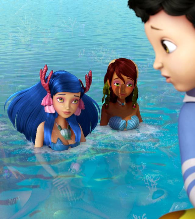 Drei Meerjungfrauen blicken aus dem Wasser hin zu Michael am Ufer.