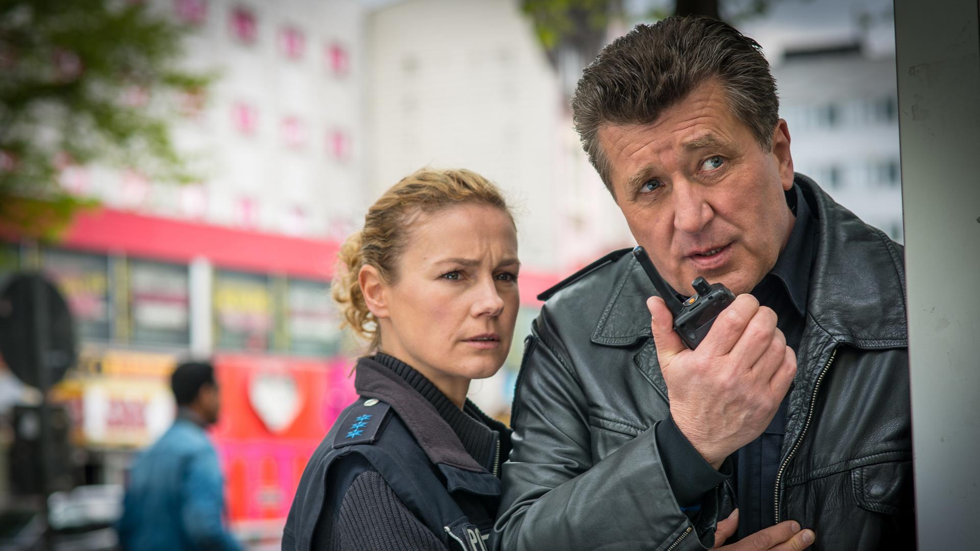 "Notruf Hafenkante - Gegen die Uhr": Die Polizeibeamten Franzi Jung (Rhea Harder-Vennewald) und Hans Moor (Bruno F. Apitz) stehen eng nebeneinander und beobachten etwas, was vor ihnen passiert. Hans hat ein Funkgerät in der Hand und spricht rein.