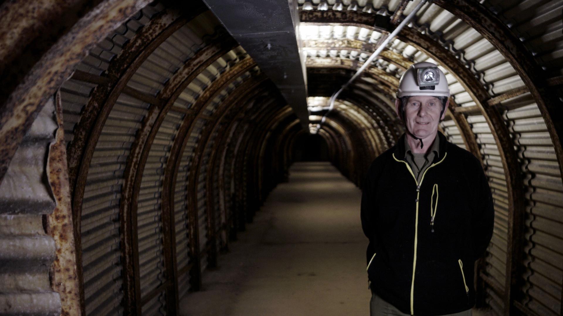 "Geheime Welten - Reise in die Tiefe: Verborgene Stollen": Mann mit Helm und Helmlampe steht in einem langen Tunnel. Der Tunnel hat ein Tonnendach.