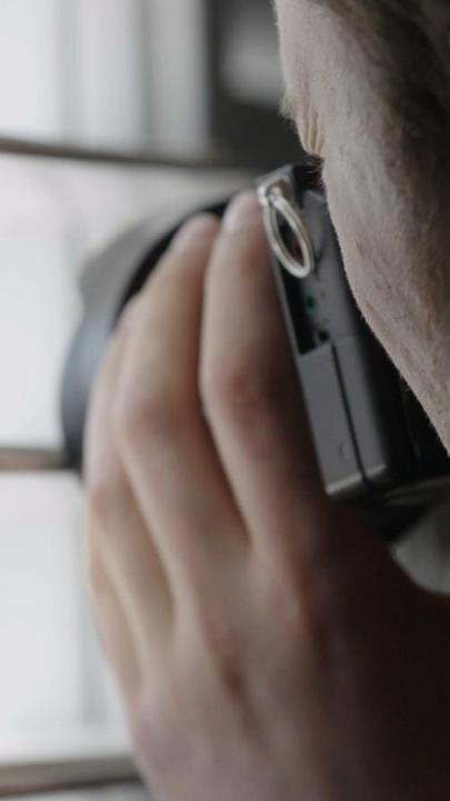 "Geheimes Israel - Der Mossad: Gefährliche Nachbarn": Ein Mann steht mit einer Kamera am Fenster und richtet das Objektiv durch die Lamellen einer Jalousie nach draußen (szenische Darstellung).