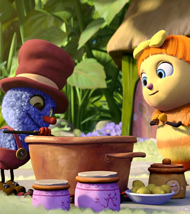 Klaus (links) probiert Josefines (rechts) Marmelade aus einem großen Marmeladentopf, der zwischen ihnen auf dem Boden steht. Josefines Gesicht sieht dabei hoffnungsvoll aus.