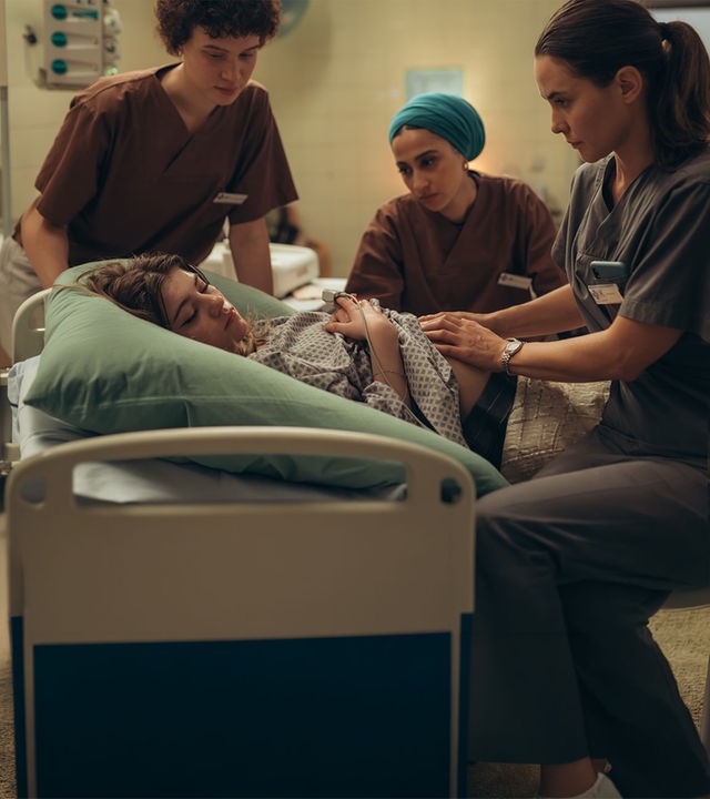 "PUSH - Geheimnisse": Lou (Lisa Moell) liegt in der Klinik. Greta (Lydia Amasko) und Meryem (Tua El-Fawwal) stehen daneben während Dr. Mohn (Katia Fellin) Lou untersucht.