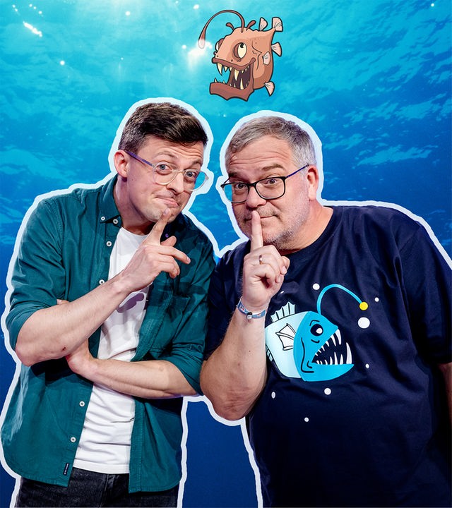 Vor einem blau schimmernden Hintergrund, der an die Tiefsee erinnert, posieren Jacob Beautemps und Elton dicht nebeneinander. Sie schauen in die Kamera und halten jeweils einen Finger an den Mund. Im rechten oberen Bereich des Bildes ist eine illustrierte, bedrohlich wirkende Meereskreatur mit leuchtendem Köder zu sehen.