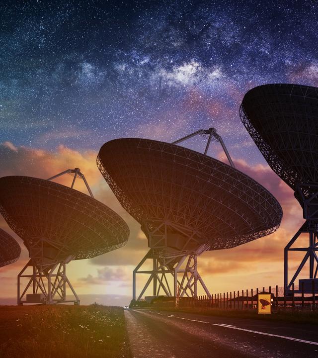 Gegen den Himmel gerichtet, stehen fünf große Radioteleskope bei Sonnenuntergang nebeneinander.