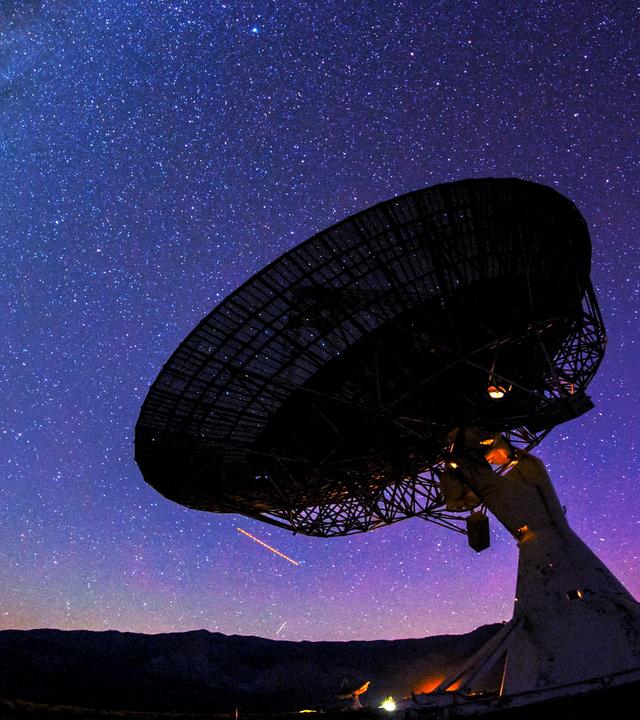 Ein riesiges Teleskop steht vor dem Nachthimmel. Dahinter ist die Milchstraße zu sehen.