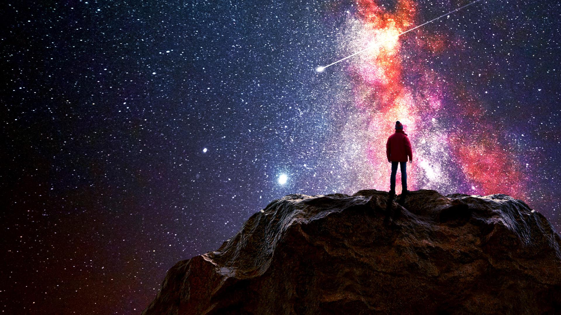 Ein Mann steht auf einem Berggipfel und beobachtet das Universum