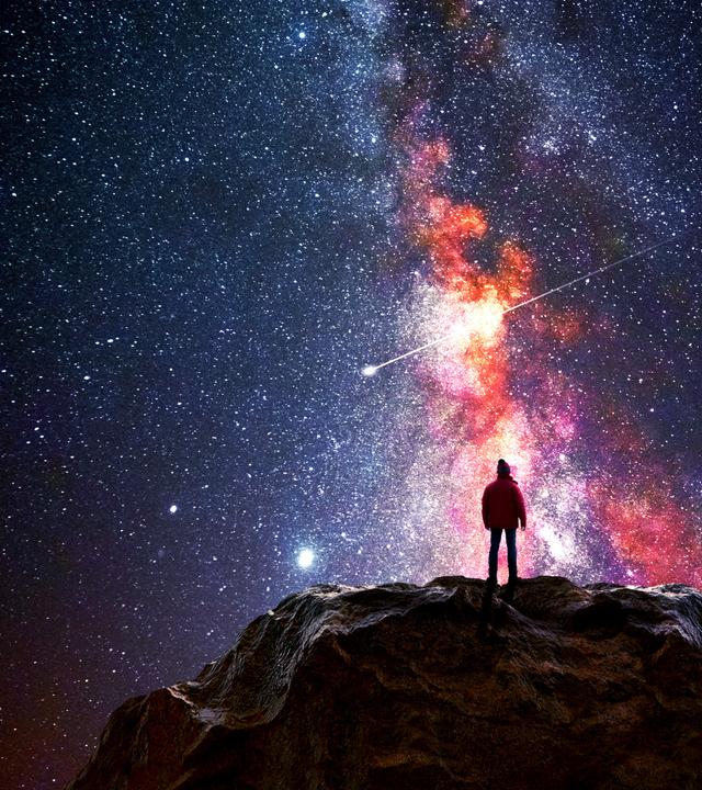 Ein Mann steht auf einem Berggipfel und beobachtet das Universum