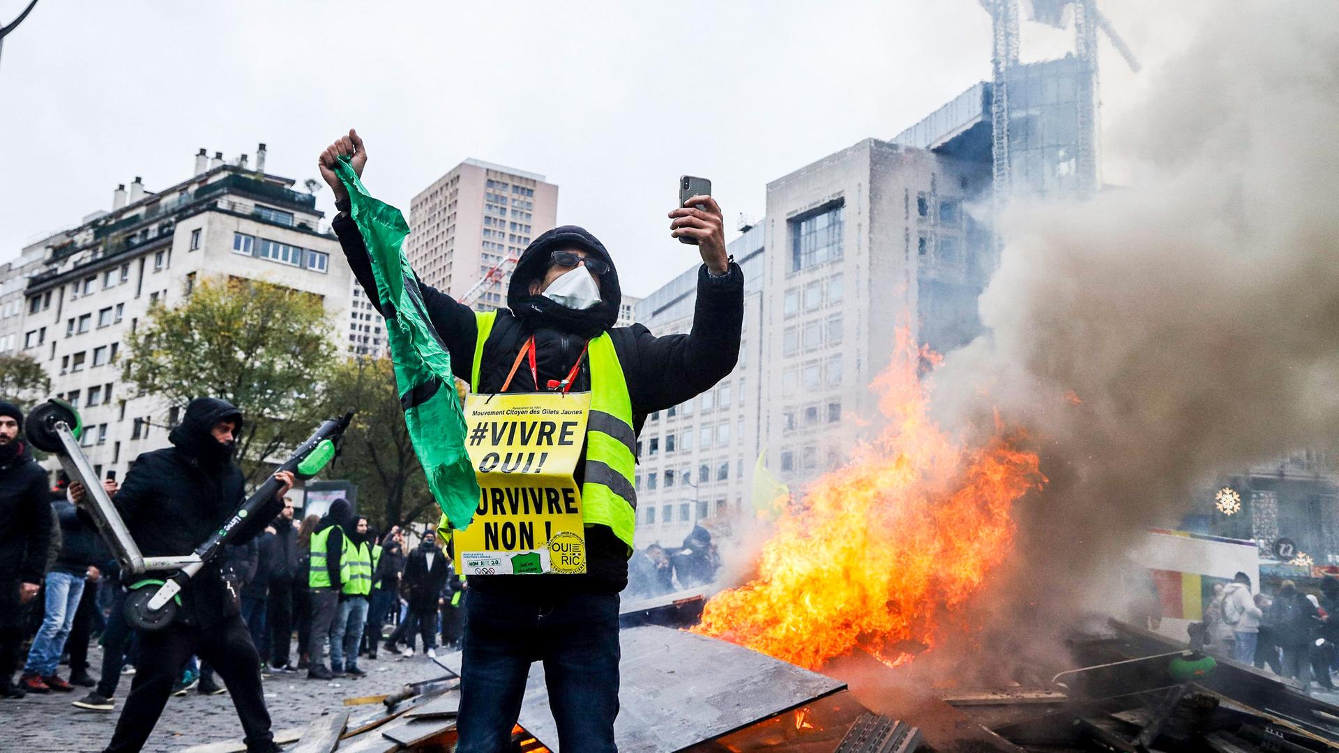 Ein vermummter Mann mit gelber Weste vor einem Feuer
