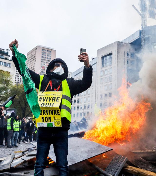Ein vermummter Mann mit gelber Weste vor einem Feuer