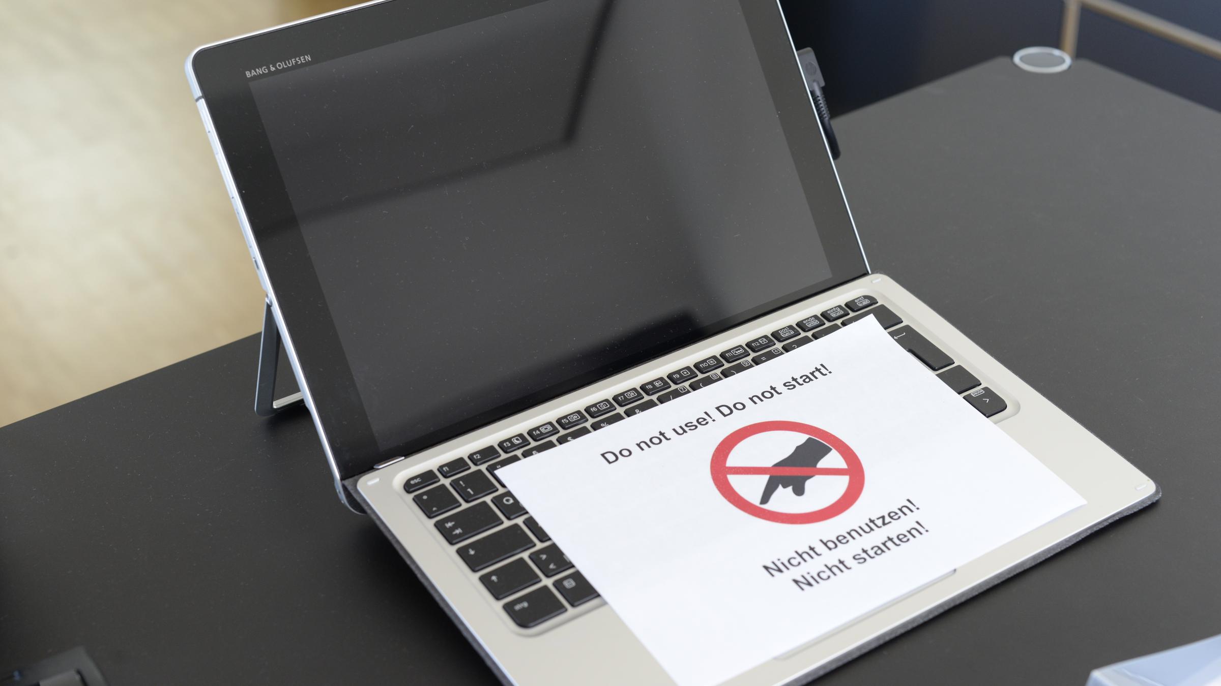 Auf einem Tisch befindet sich ein geöffneter Laptop mit schwarzem Bild. Darauf liegt ein Zettel mit dem Hinweis "Nicht benutzen!" und einer rot durchgestrichenen Hand.