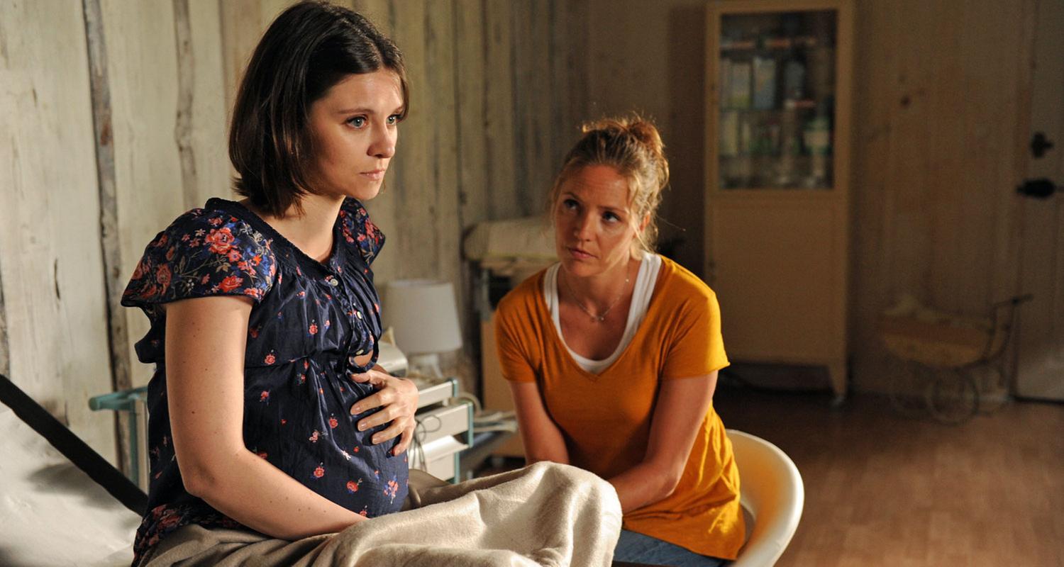 "Lena Lorenz - Geliehenes Glück": Die hochschwangere Katerina Nowak (Natalia Rudziewicz) sitzt auf einer Liege in der Hebammenpraxis. Bei ihr sitzt Lena Lorenz (Patricia Aulitzky) und beobachtet die junge Frau.