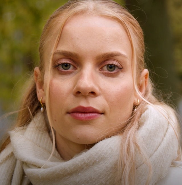 Im Zentrum des Bildes eine junge Frau mit blonden Haaren, die in die Kamera blickt