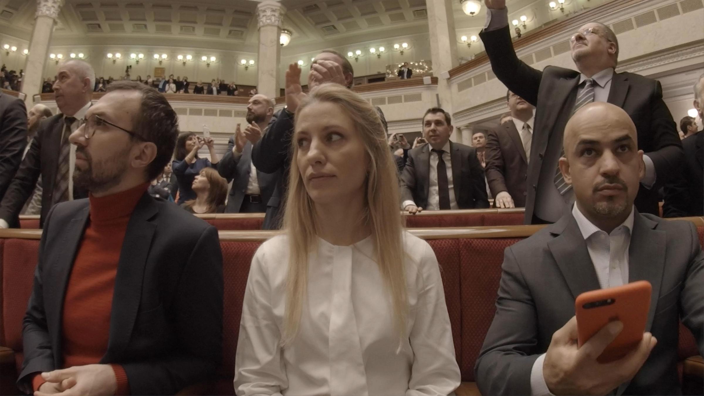 "Generation Euromaidan - Sehnsucht nach Demokratie": Serhij Leschtschenko, Switlana Salischtschuk und Mustafa Najjem sitzen angespannt nebeneinander. Im Hintergrund sieht man stehende Männer in Anzügen.