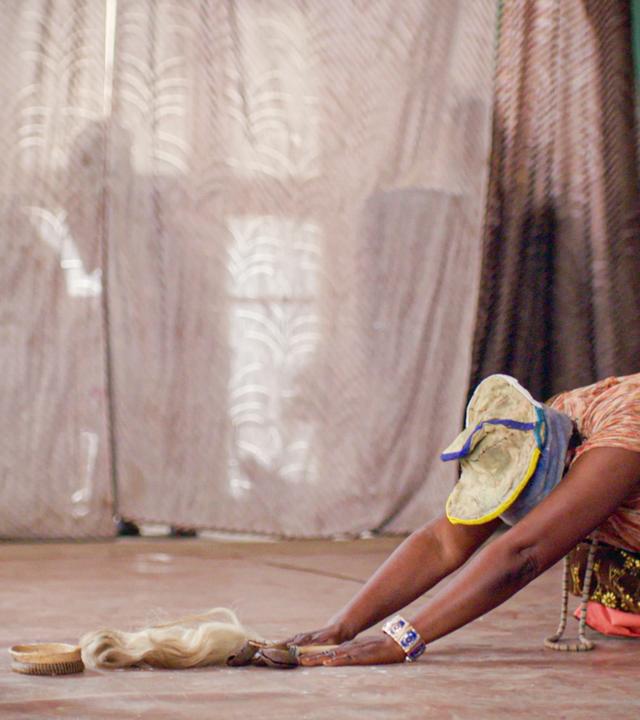 Eine Frau verneigt sich auf Knien vor einer Holzfigur und weiteren Objekten