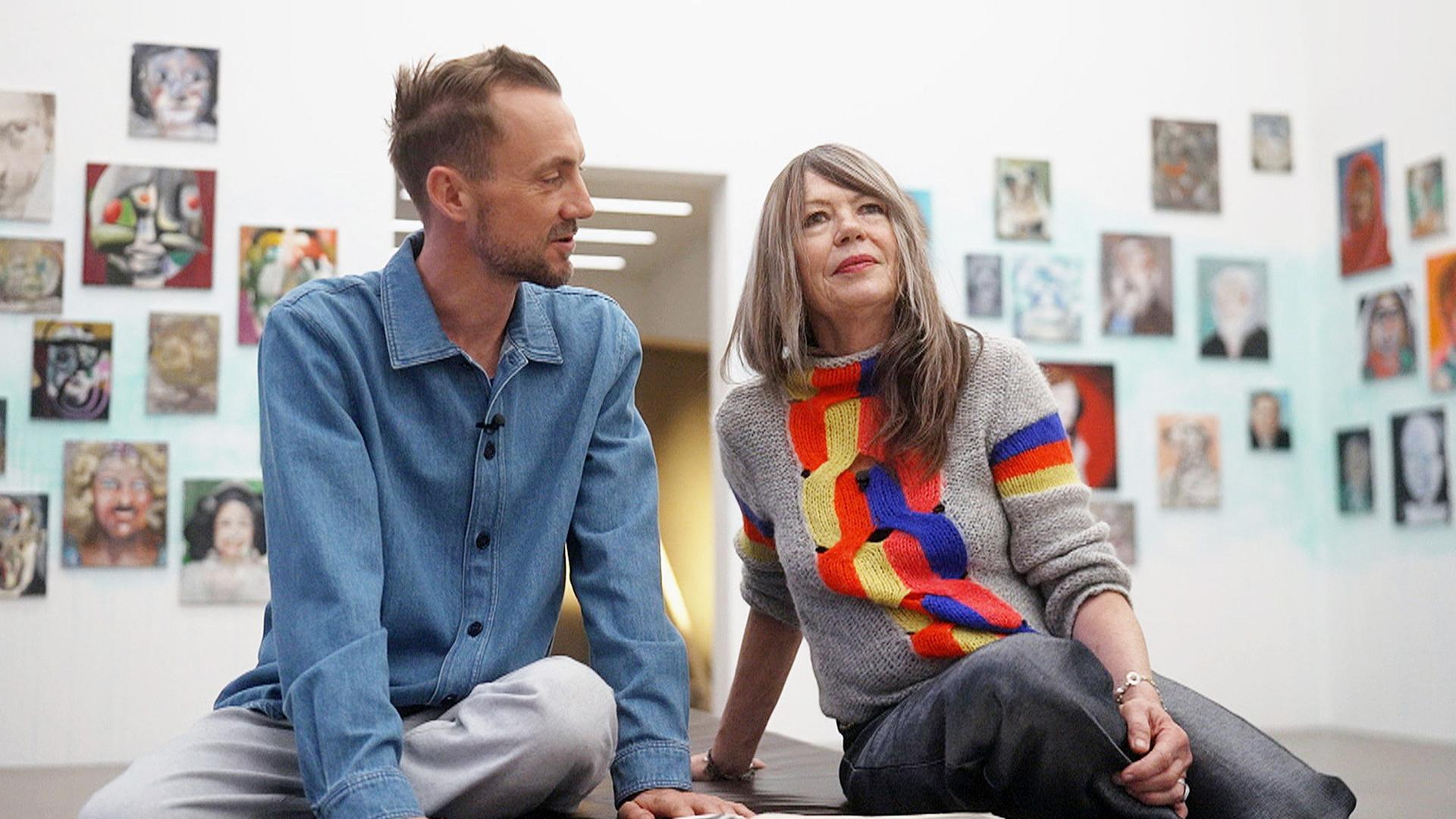 Ein Mann und eine Frau sitzen vor einer Wand mit vielen Bildern