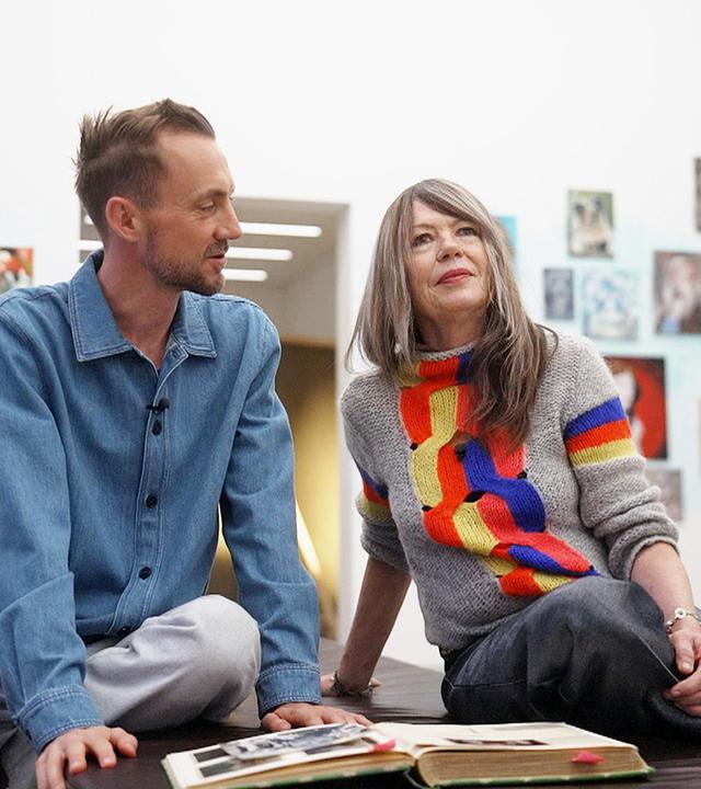 Ein Mann und eine Frau sitzen vor einer Wand mit vielen Bildern