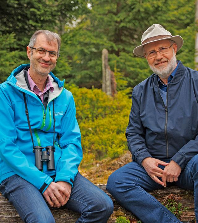 Harald Lesch und Jörg Müller sitzen auf einem Baumstamm im Wald