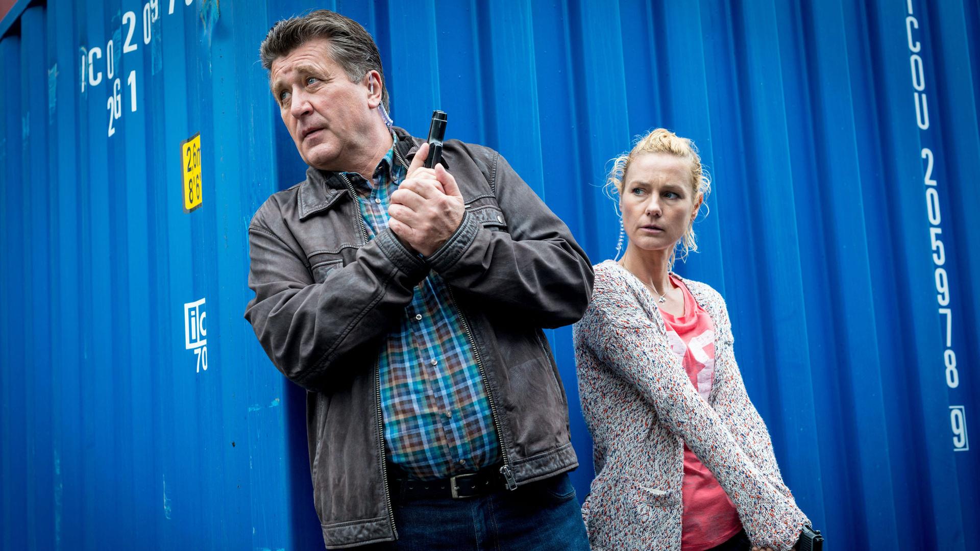 "Notruf Hafenkante - Gestohlenes Leben": Hans Moor (Bruno F. Apitz) und Franzi Jung (Rhea Harder-Vennewald) stehen in Deckung hinter einem blauen Container. Beide halten ihre Waffen einsatzbereit. Sie sind in Zivil.