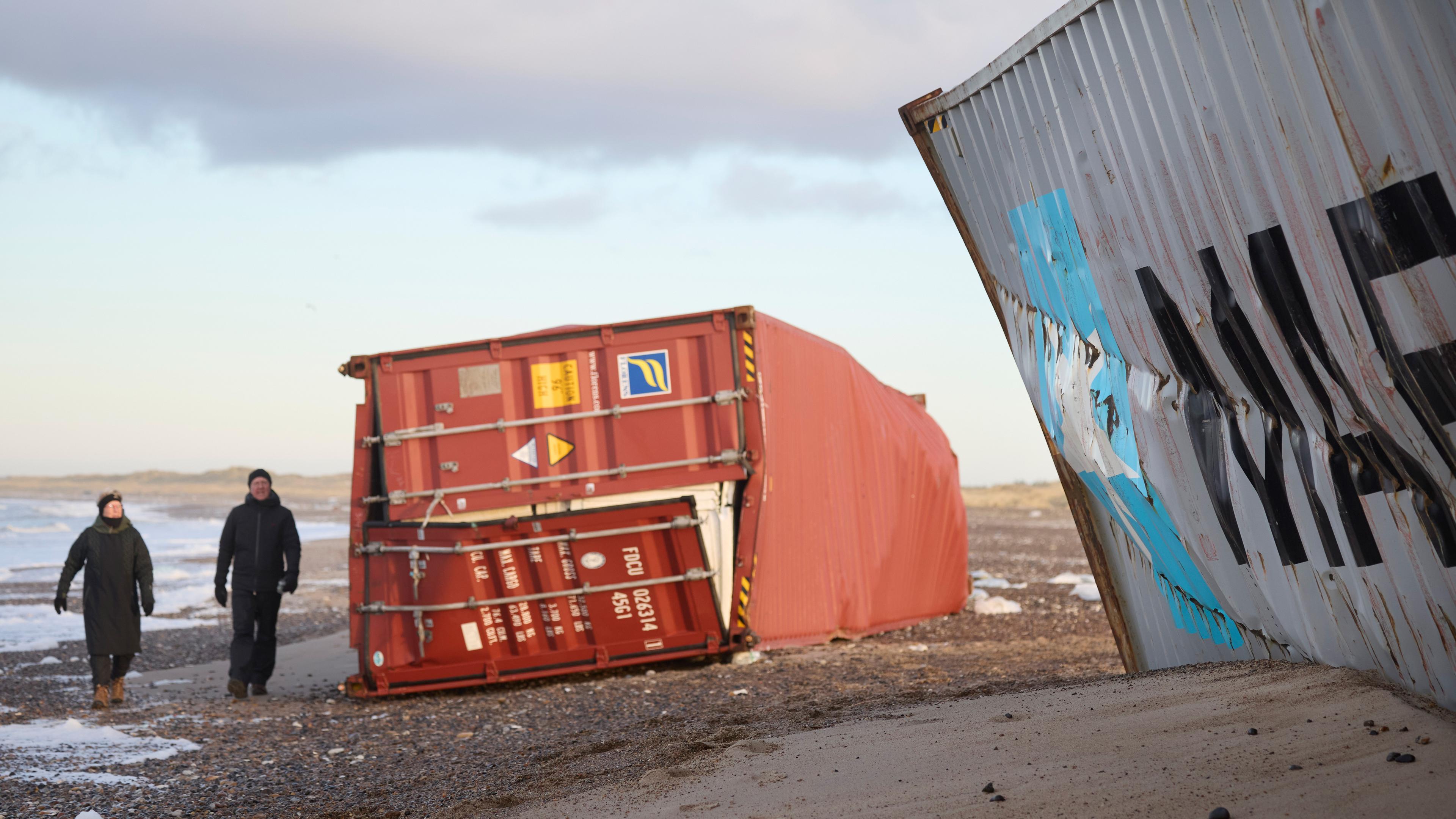 Menschen gehen an gestrandeten Containern in der Gegend zwischen Tranum und Slette Strand in Dänemark vorbei, aufgenommen am 23.12.2023