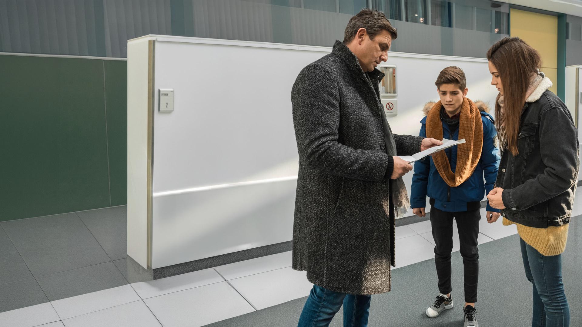 "Der Bergdoktor: Getrennte Wege (2)": Hans Sigl (Dr. Martin Gruber) steht im Krankenhaus mit Mara (Ava Montgomery) und ihrem Freund Leon (Juls Luis Serger) zusammen. Hans hält Papiere in der Hand, auf die die beiden Jugendlichen besorgt schauen.