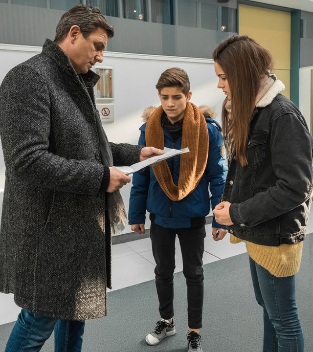 "Der Bergdoktor: Getrennte Wege (2)": Hans Sigl (Dr. Martin Gruber) steht im Krankenhaus mit Mara (Ava Montgomery) und ihrem Freund Leon (Juls Luis Serger) zusammen. Hans hält Papiere in der Hand, auf die die beiden Jugendlichen besorgt schauen.