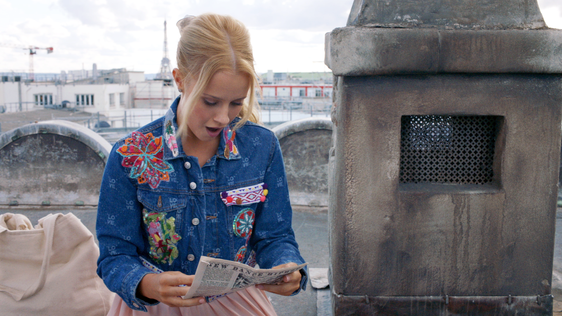 Lena sitzt auf dem Dach der Pariser Oper und liest eine Zeitung. Sie sieht geschockt aus.