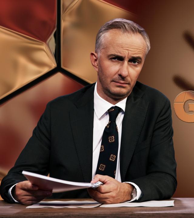 Jan Böhmermann sitzt am Schreibtisch. Rechts von ihm ist der Schatten einer erhobenen Hand vor einem braunen Hintergrund zu sehen. Auf der Hand steht in Großbuchstaben "Häusliche Gewalt".