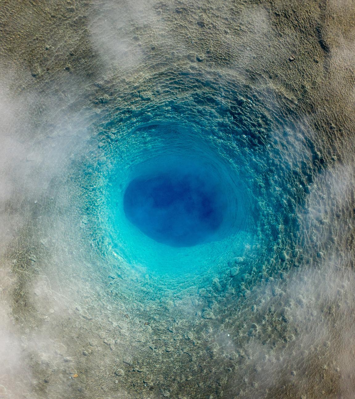 Blick von oben auf einen ruhenden Geysir, der aussieht, wie ein blauer Wirbel.