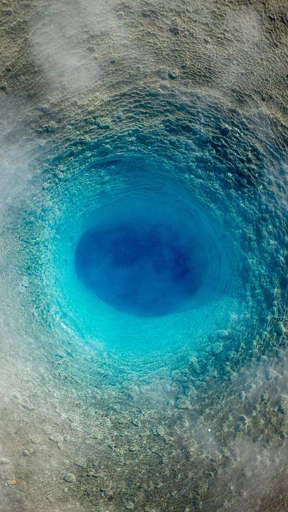 Blick von oben auf einen ruhenden Geysir, der aussieht, wie ein blauer Wirbel.