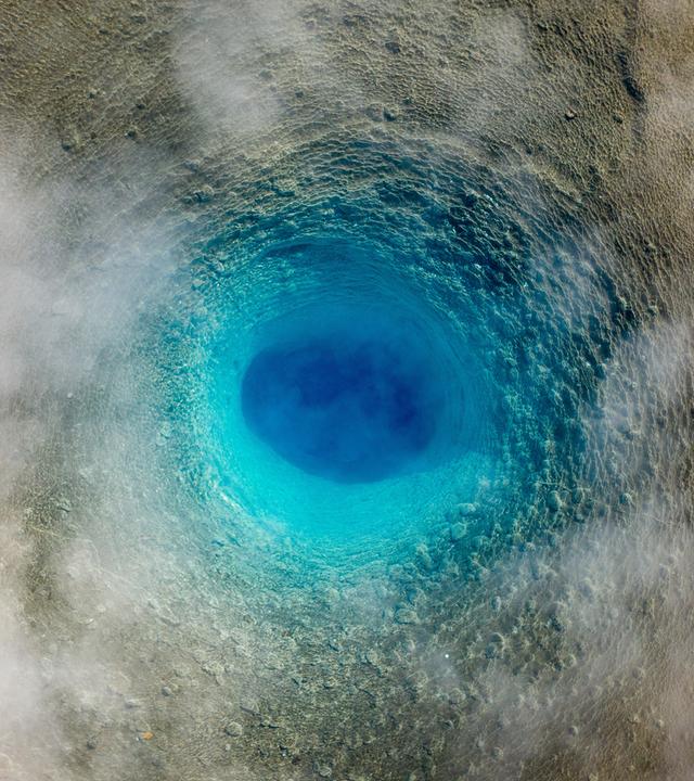 Blick von oben auf einen ruhenden Geysir, der aussieht, wie ein blauer Wirbel.