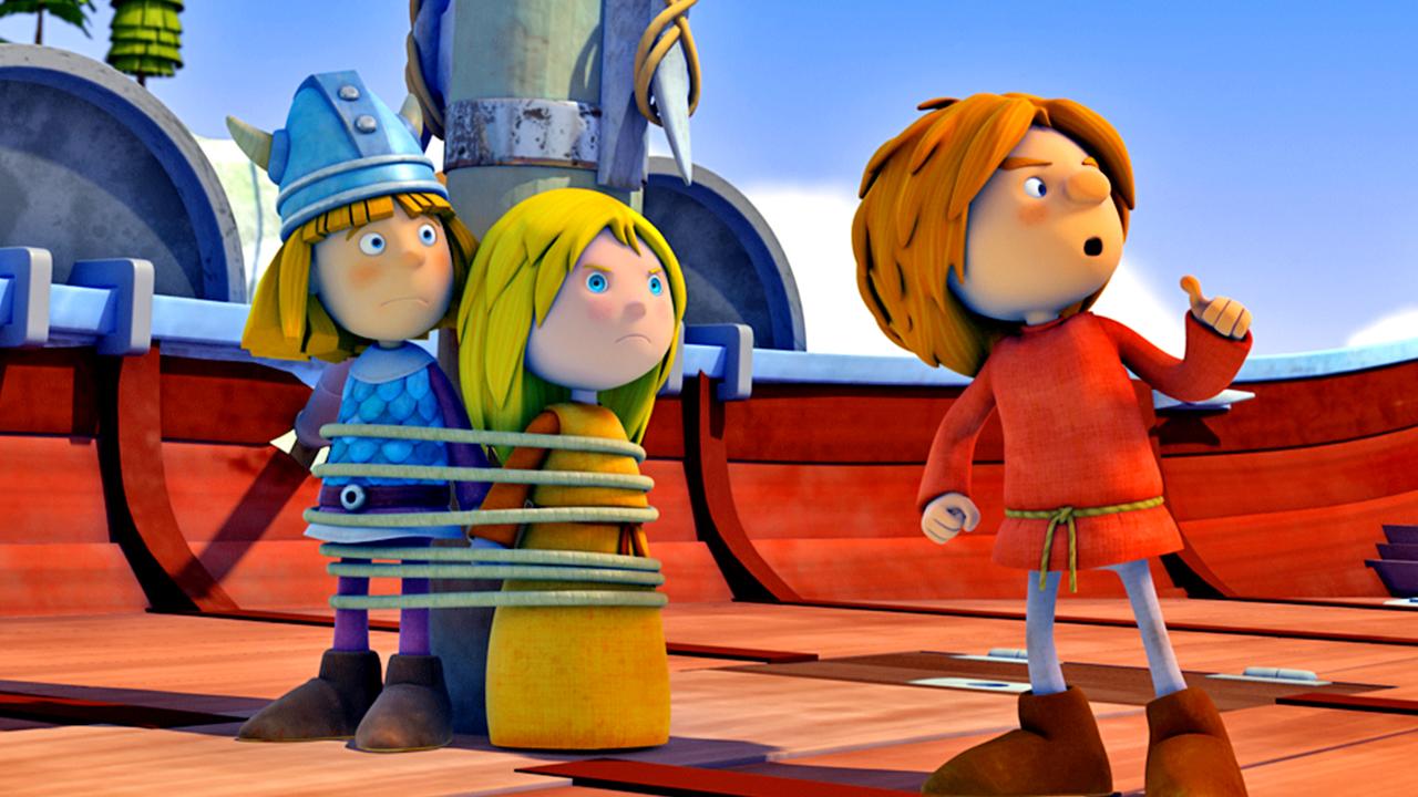 Wickie und Ilvy sind mit einem Seil am Mast festgebunden. Wickie wirkt überrascht, Ilvy sieht grimmig aus. Rechts neben ihnen steht Gilby. Alle schauen nach rechts. Im Hintergrund stehen weitere Wikingerkinder, die Gilby geschockt ansehen.