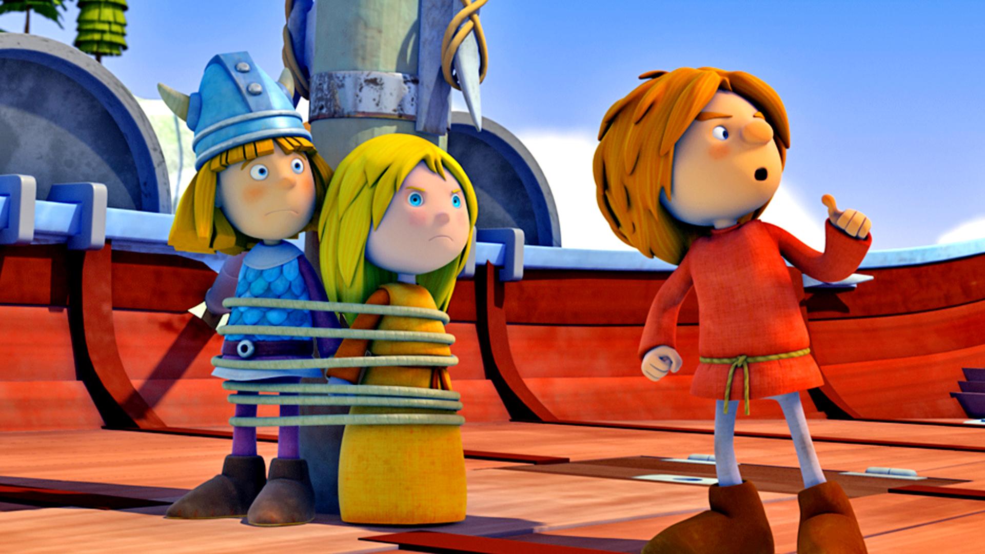 Wickie und Ilvy sind mit einem Seil am Mast festgebunden. Wickie wirkt überrascht, Ilvy sieht grimmig aus. Rechts neben ihnen steht Gilby. Alle schauen nach rechts. Im Hintergrund stehen weitere Wikingerkinder, die Gilby geschockt ansehen.