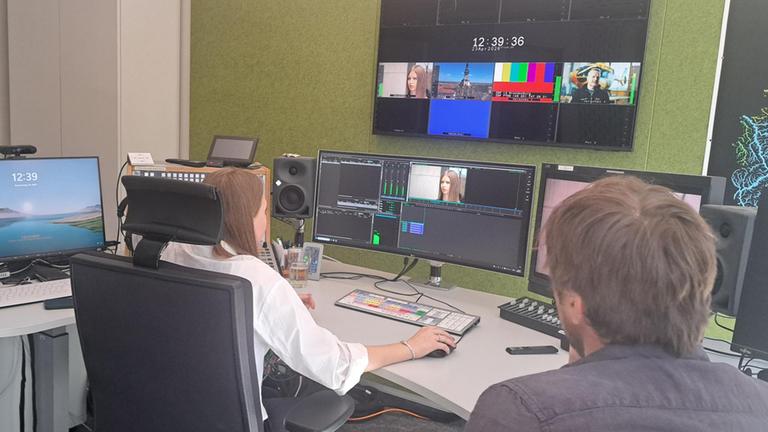 Eine Schülerin sitzt an einem professionellen Videoschnittplatz im ZDF-Studio Potsdam und arbeitet an mehreren Monitoren mit Schnittsoftware. Neben ihr unterstützt ein Mitarbeiter, während sie beim Girls’ Day 2026 Einblicke in die Postproduktion erhält.