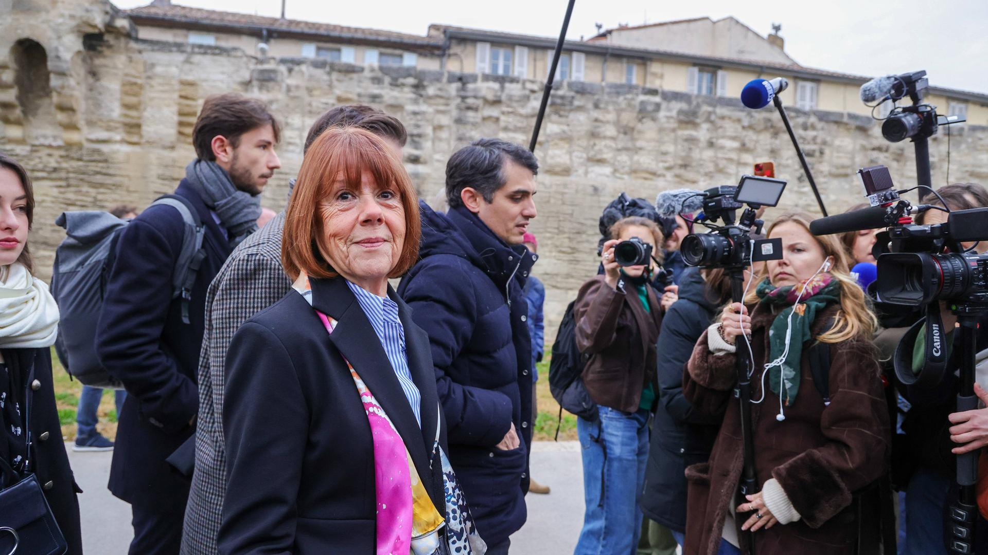 Eine Frau ist umringt von Reportern und Reporterinnen.