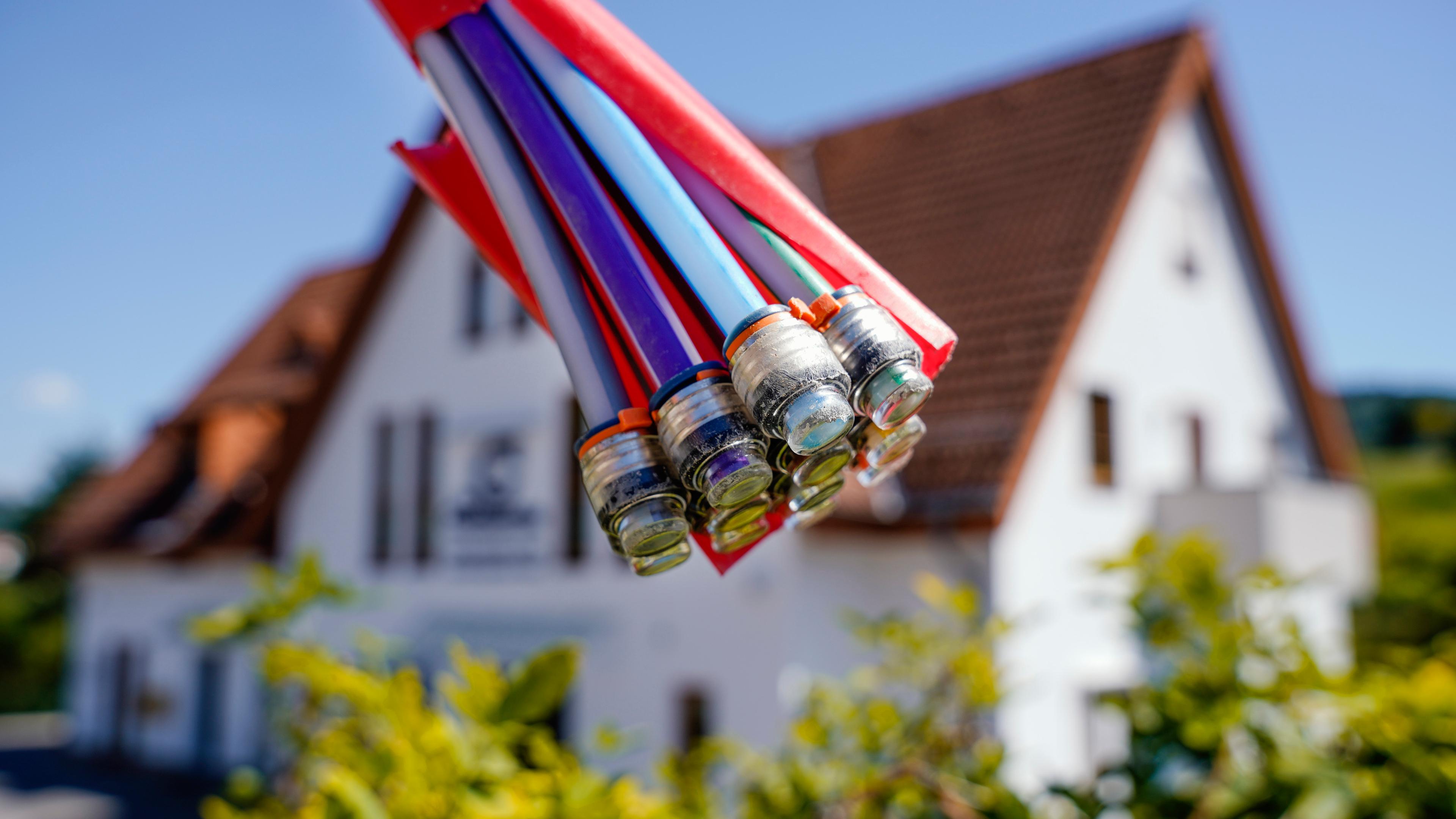 Ein Bündel Glasfaser-Kabel werden vor einem Haus hochgehalten.