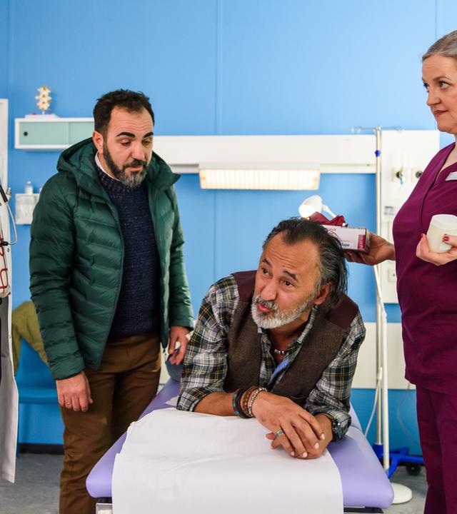 "Bettys Diagnose - Glatteis": Safi Edemir (Ercan Durmaz) liegt bäuchlings als Patient von Dr. Helena von Arnstett (Claudia Hiersche) auf einer Liege, Mechthild Puhl (Sybille J. Schedwill) assistiert und sein Bruder Emre Edemir (Adnan Maral) steht neben ihm.