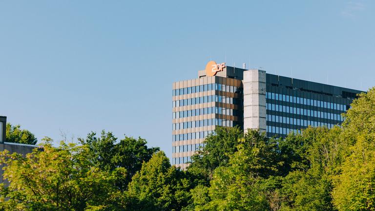 Typical ZDF: Das ZDF Hochaus mit dem Logo auf dem Mainter Lerchenberg aus der Ferne mit Bäumen davor