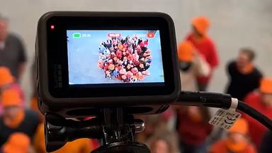 Screenhot aus dem ZDF LinkedIn-Post zu den Orange Days im ZDF: Blick auf ein Kameradisplay, in dem eine Menschengruppe mit orangefarbenen Hüten in die Kamera blickt