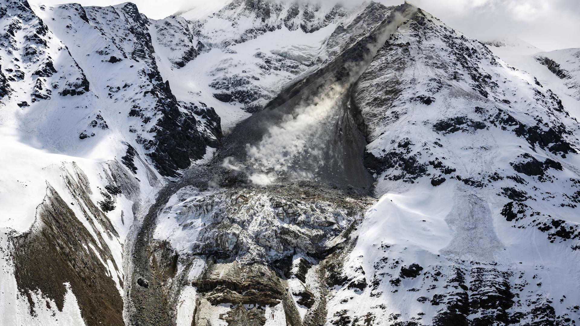 Eine Lawine aus Geröll und Eis geht zwischen schneebedeckten Bergen ab.
