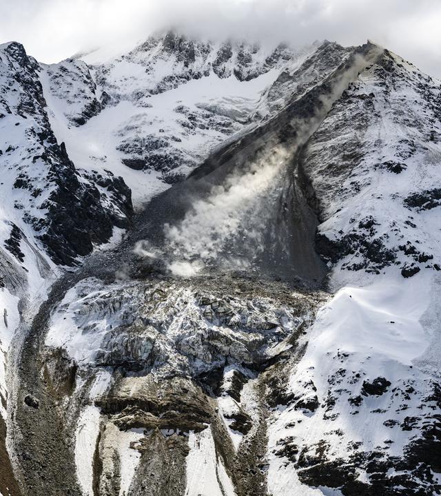 Eine Lawine aus Geröll und Eis geht zwischen schneebedeckten Bergen ab.