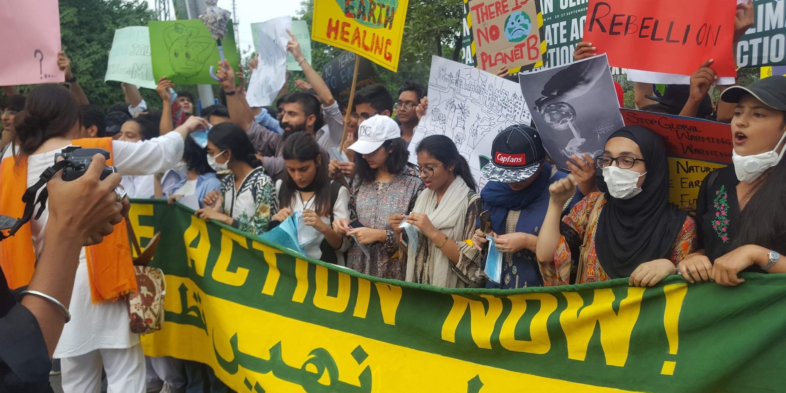 Junge Menschen, vor allem Mädchen, halten ein Banner und mehrere Schilder, die ein Handeln gegen den Klimawandel fordern. Einige tragen eine Gesichtsmaske.