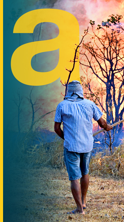 Mann steht mit Schippe und Rücken zum Beobachter. Rechts nebendran ist ein Waldbrand