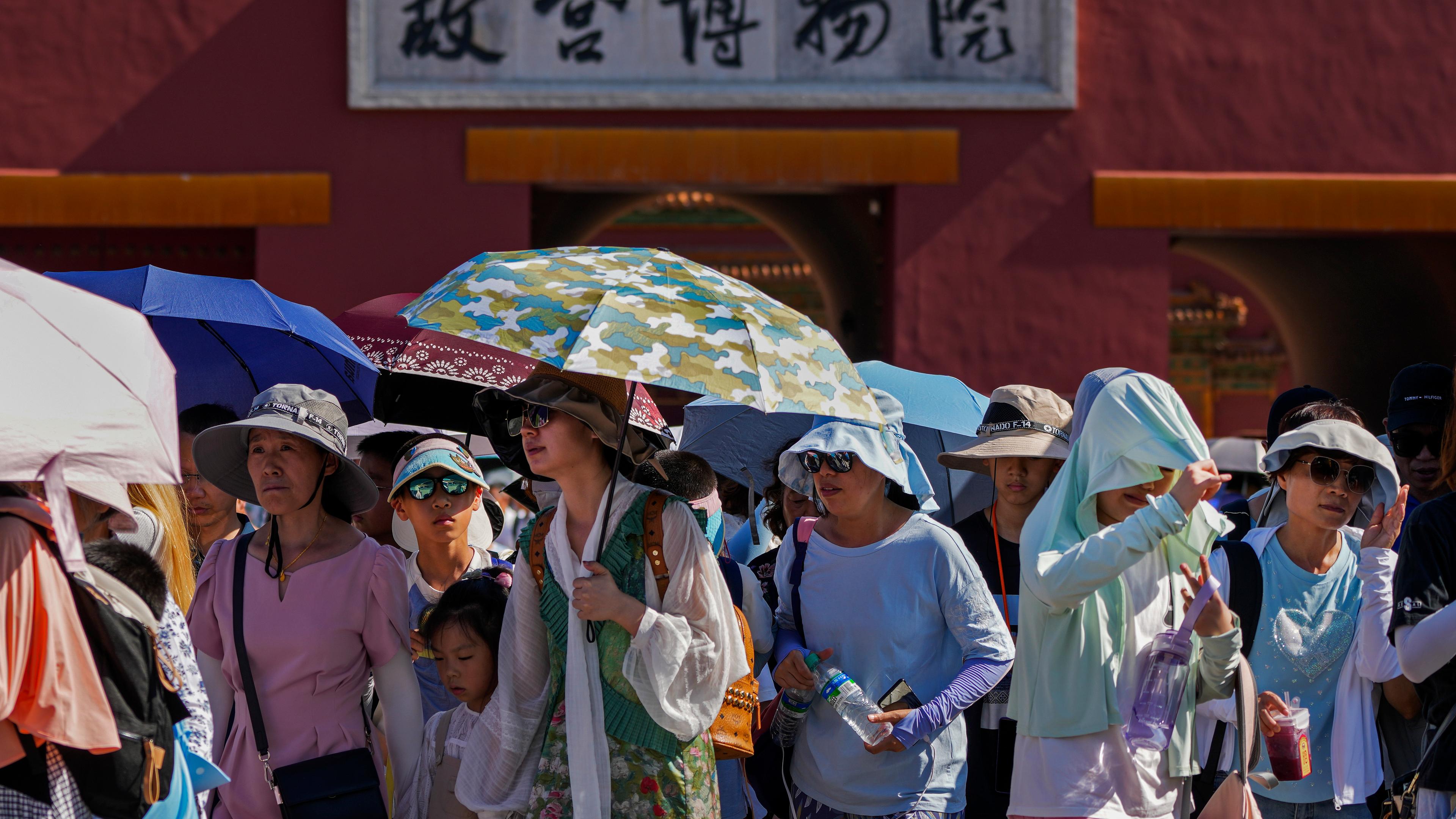 Zu sehen sind Menschen in Peking, die sich mit Schirmen und Hüten vor der Hitze schützen.