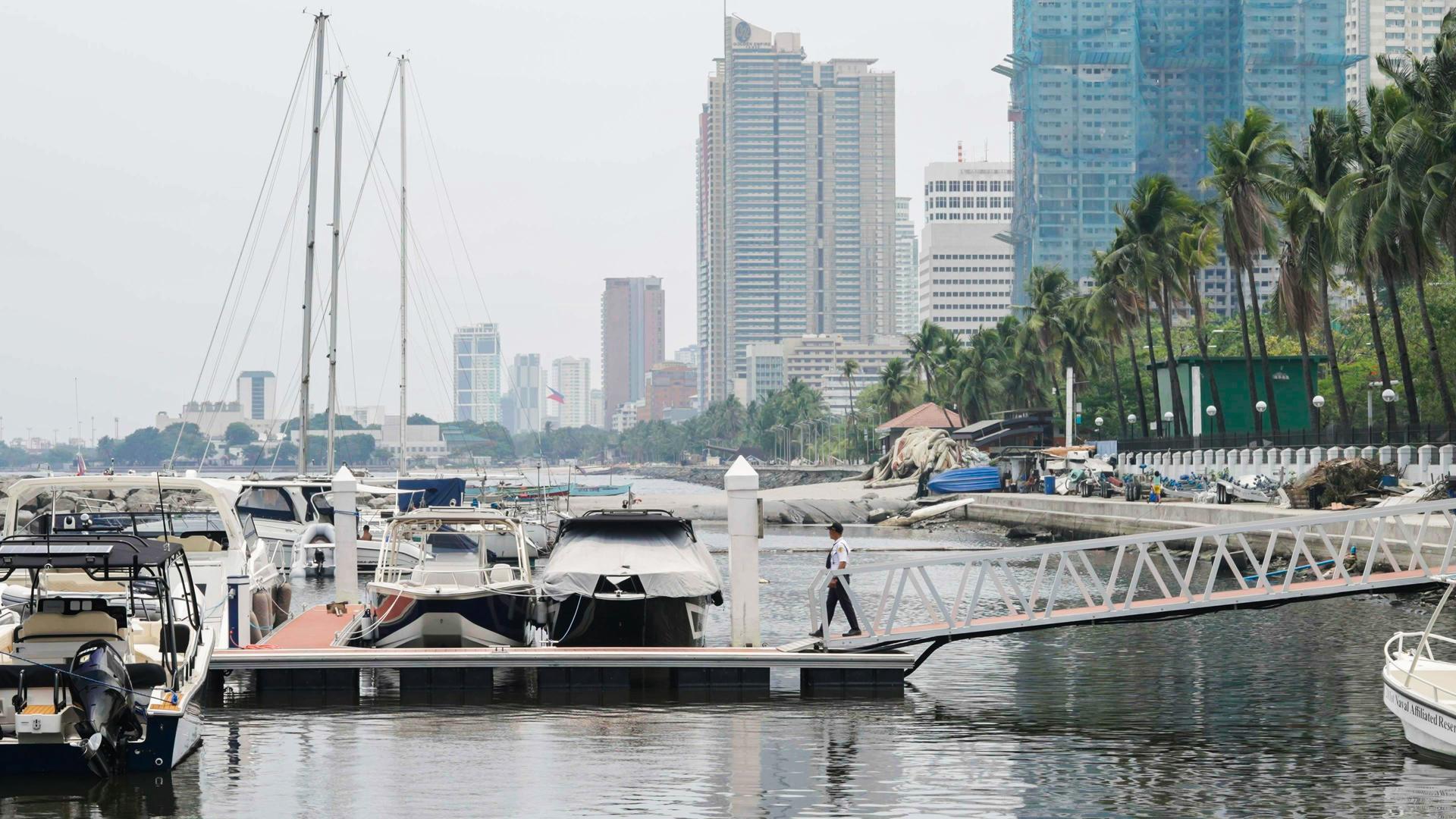 Blick auf den Jachthafen von Manila mit mehreren Booten am Anleger, Palmen am Ufer und Hochhäusern im Hintergrund