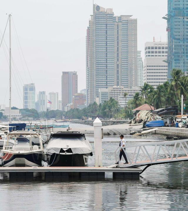 Blick auf den Jachthafen von Manila mit mehreren Booten am Anleger, Palmen am Ufer und Hochhäusern im Hintergrund