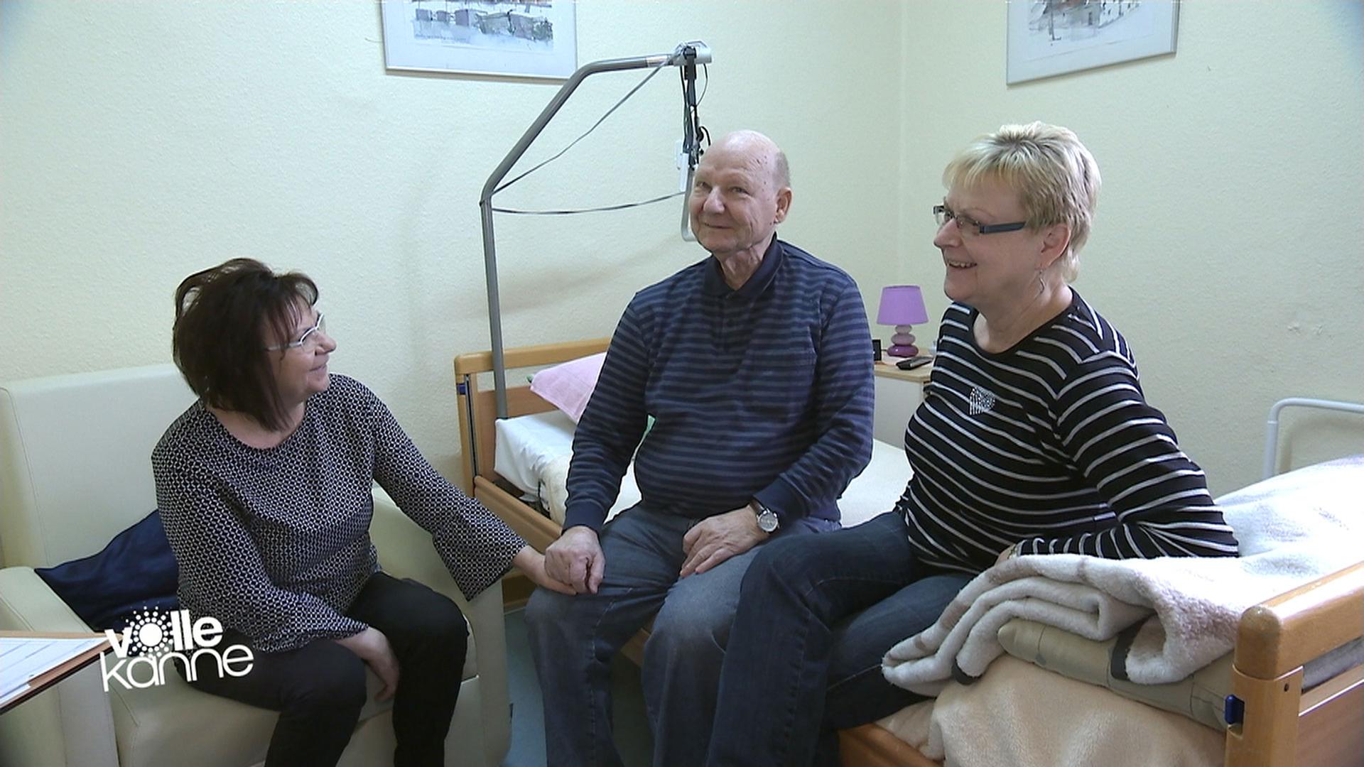 Drei Personen sitzen auf einem Krankenbett.