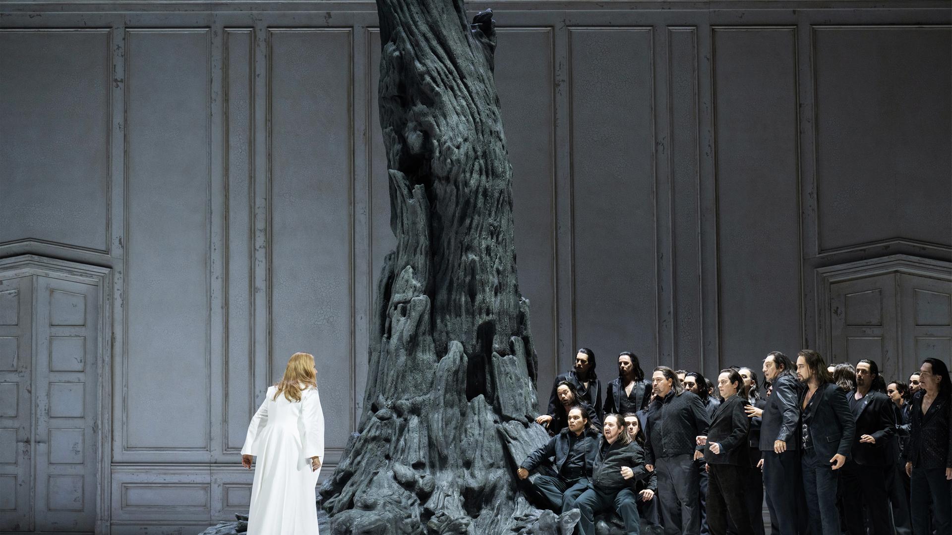 Eine dunkel gekleidetet Menschenmenge steht einer Frau im weissen Kleid gegenüber