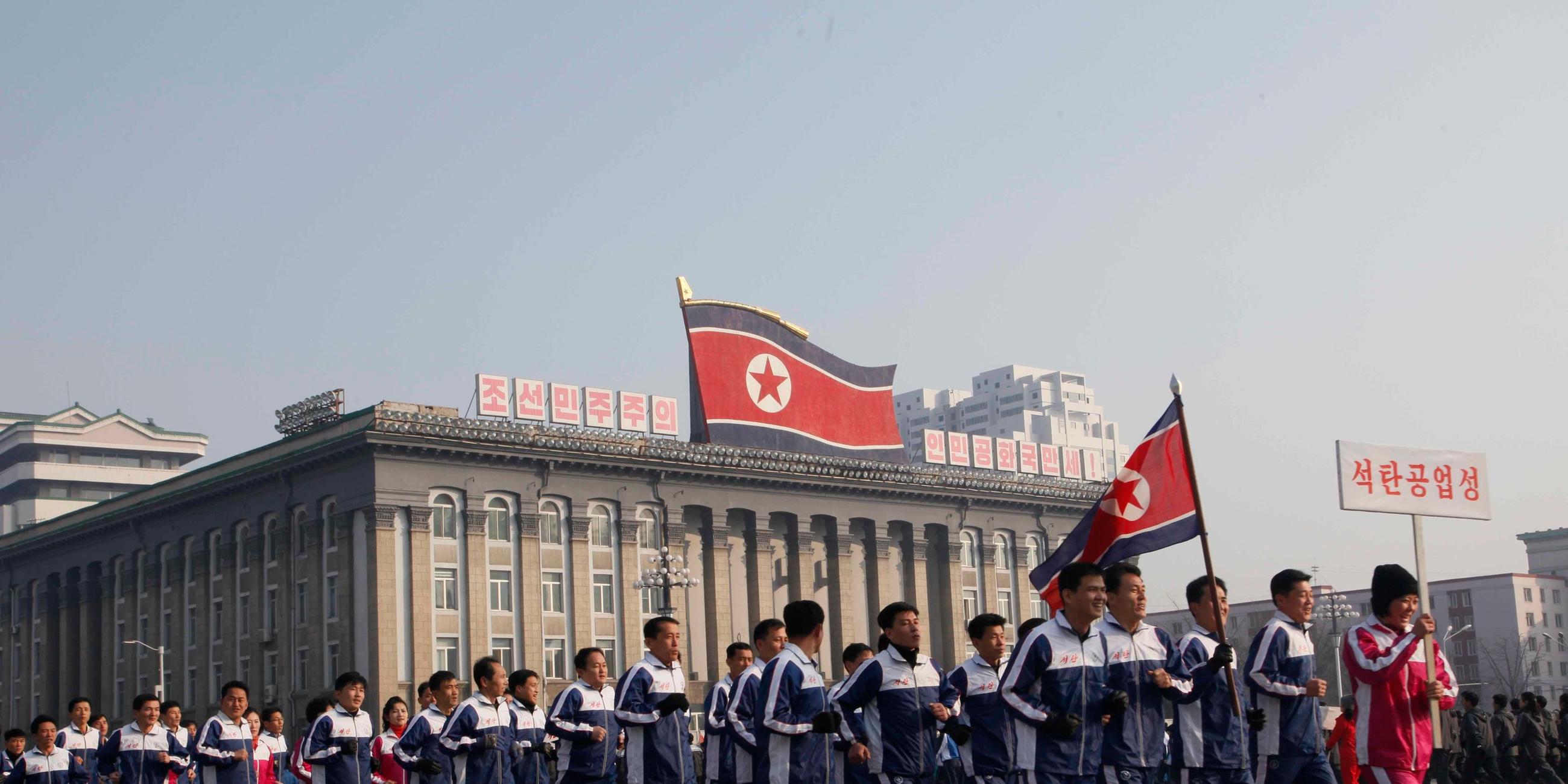Eine Gruppe nordkoreanischer Regierungsbeamter joggt in Pjoengjang über den Kim-Il-Sung-Platz.